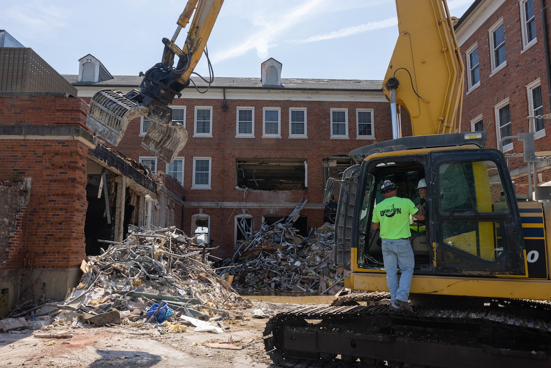 Ronald “Boots” Feather, owner of Demolition Services Incorporated, assists U.S. Marine Corps Col. Jenny Colegate, commanding officer of Marine Corps Base Quantico, with the demolition of Robinson Hall on MCB Quantico, Virginia, July 29, 2025. Robinson Hall is being demolished in order to continue safe flight operations aboard Marine Corps Air Facilities Quantico. A former bachelor enlisted barracks, it was built in 1940 and was named after 1st Lt. Robert Guy Robinson, who was awarded the Purple Heart and Medal of Honor during World War I. (U.S. Marine Corps photo by Lance Cpl. David Brandes)