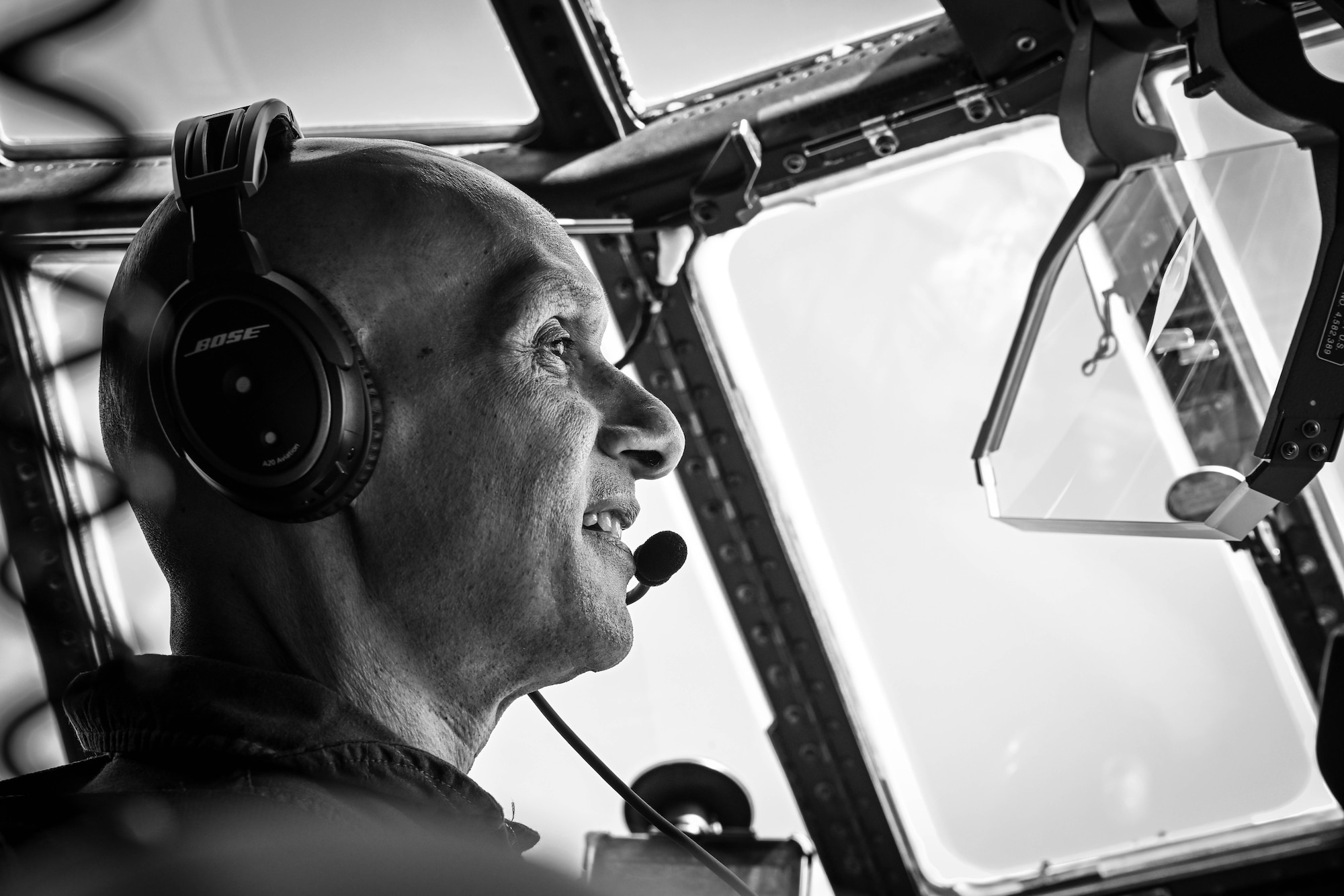 A man in uniform looks out the window while flying a plane.
