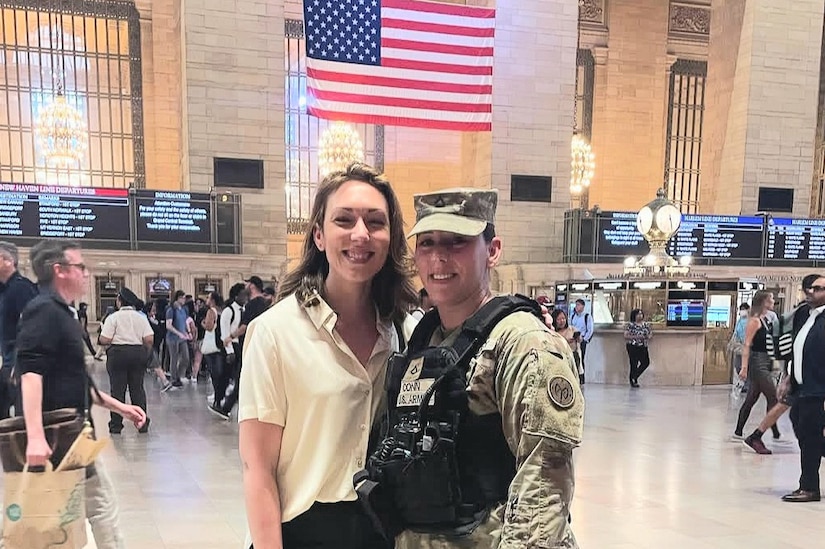 A woman in uniform poses next to a woman in civilian attire in the lobby of a train station.