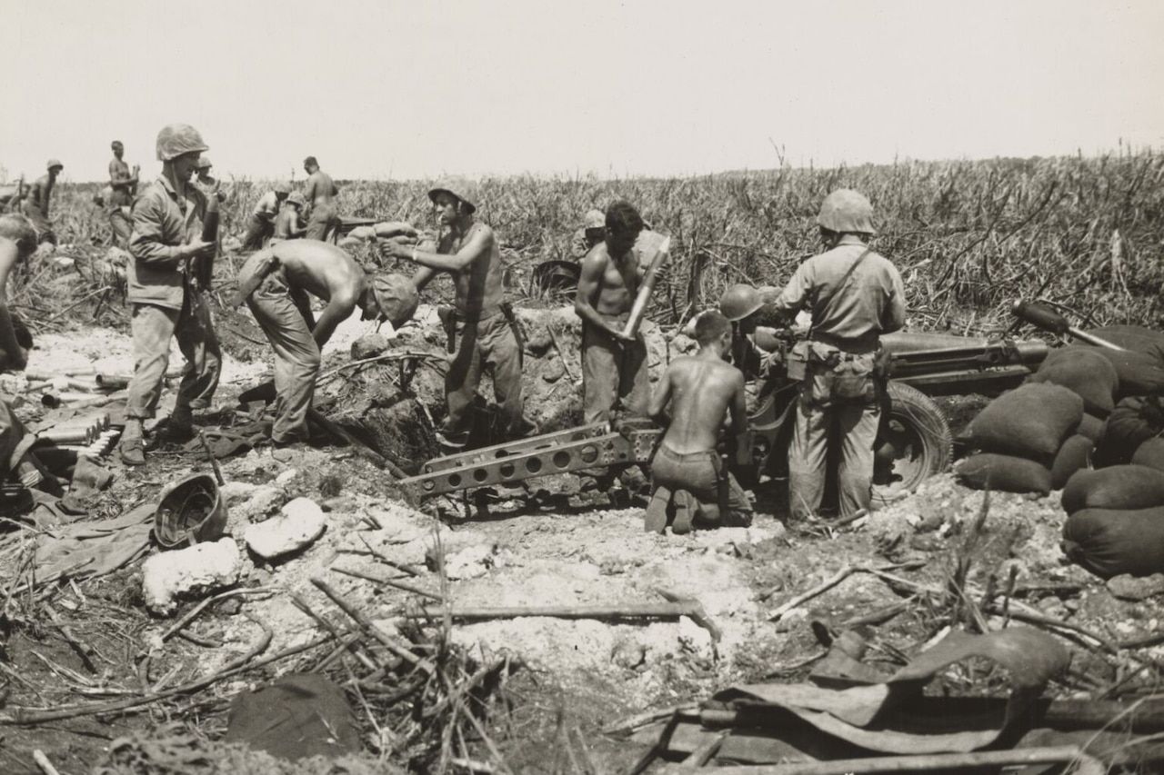Several men work to put together a large weapon in thick grass.