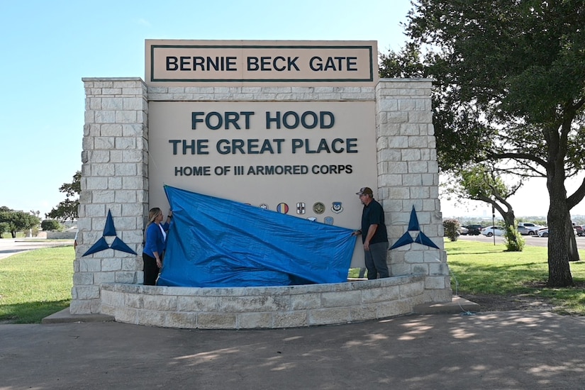 Workers remove a tarp from a sign, revealing the words "Fort Hood, the Great Place."