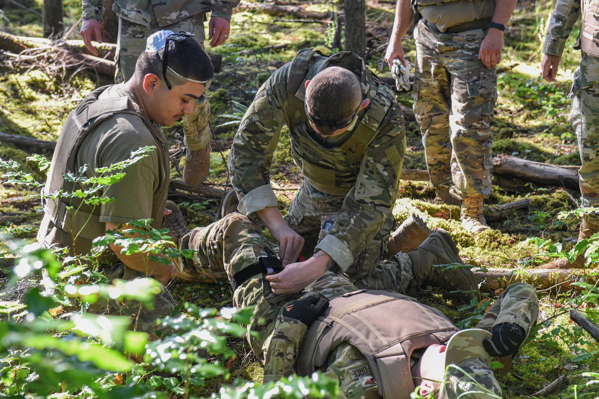 U.S. Air Force Senior Airman Alizeh Lopez, left, and Staff Sgt. Hunter Campbell, both Julius A. Kolb Airman Leadership School class 25-E students, apply a tourniquet to a simulated injured classmate during an ALS field exercise at Joint Base Lewis-McChord, Washington, July 8, 2025.