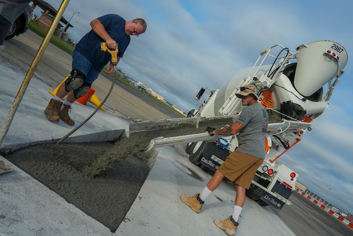 78th Civil Engineer Squadron masons Robert Wreden directs concrete into a taxiway repair hole while Travis Murphy aerates the mix at Robins Air Force Base, Georgia, July 24th, 2025.