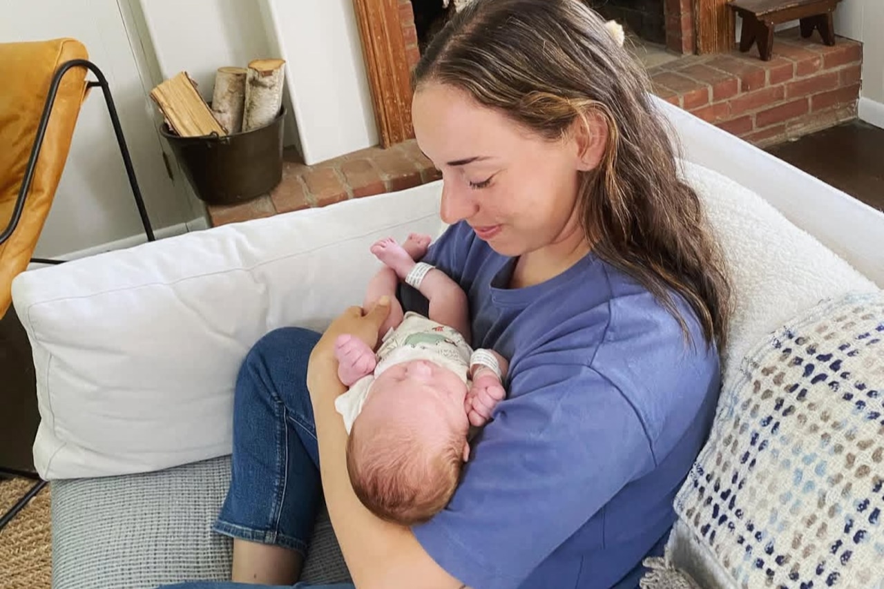 A woman holds a baby while sitting on a couch in a room.
