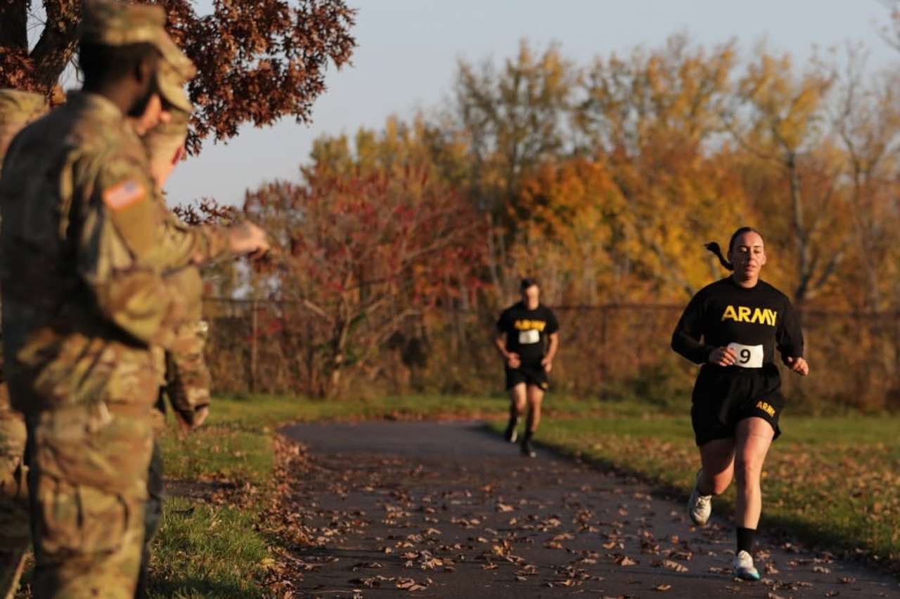 A female guardsman runs on a trail as other service members look on.