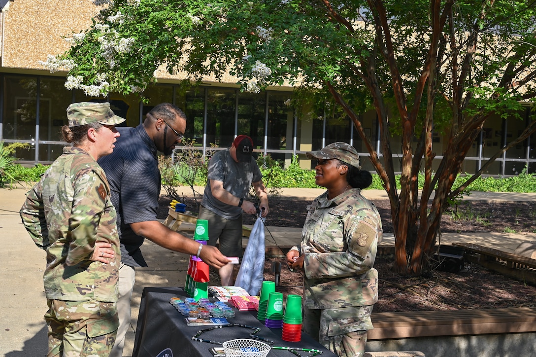 People in uniform talk around a table full of resources at an outdoor BBQ.
