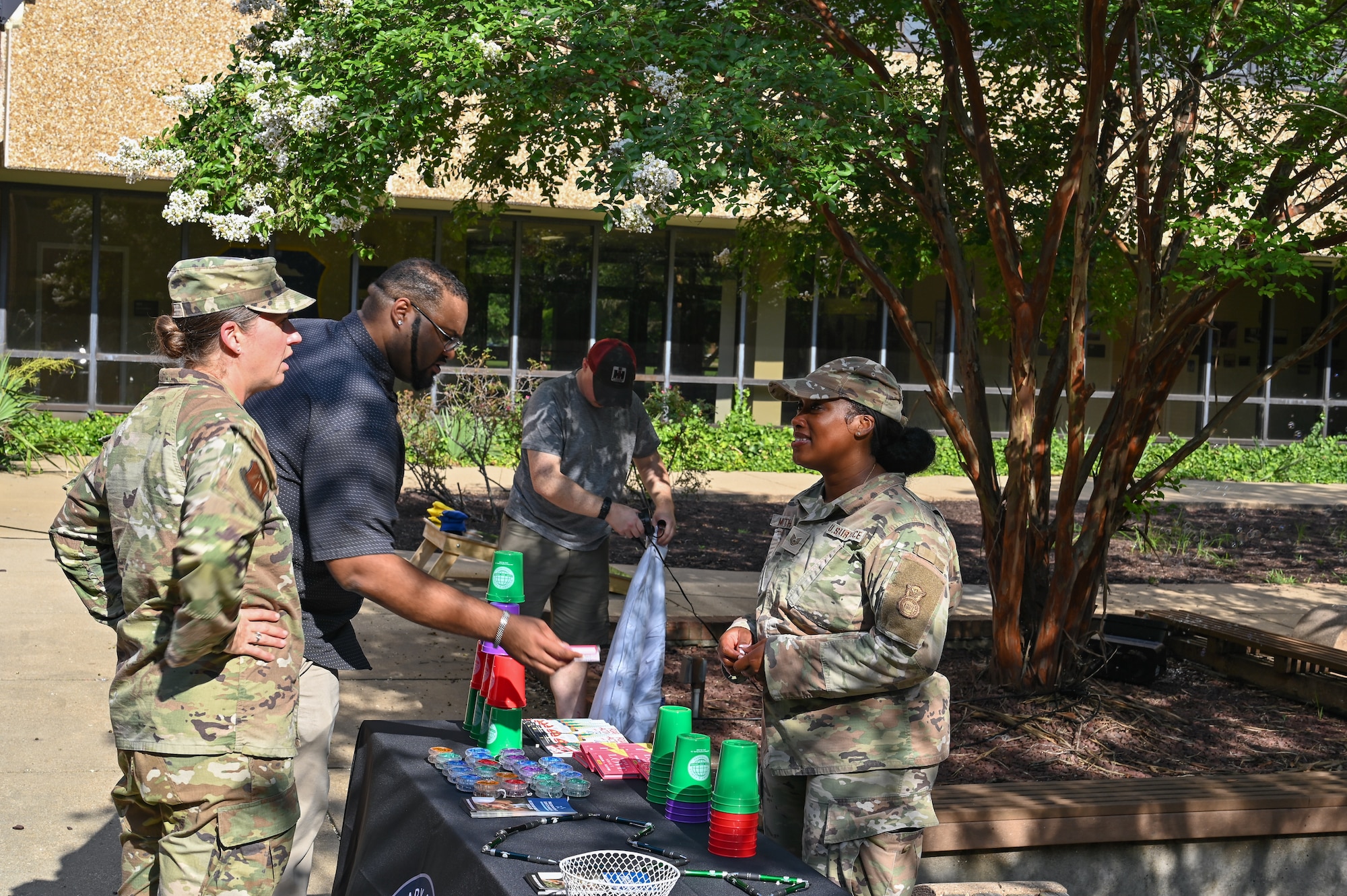 People in uniform talk around a table full of resources at an outdoor BBQ.