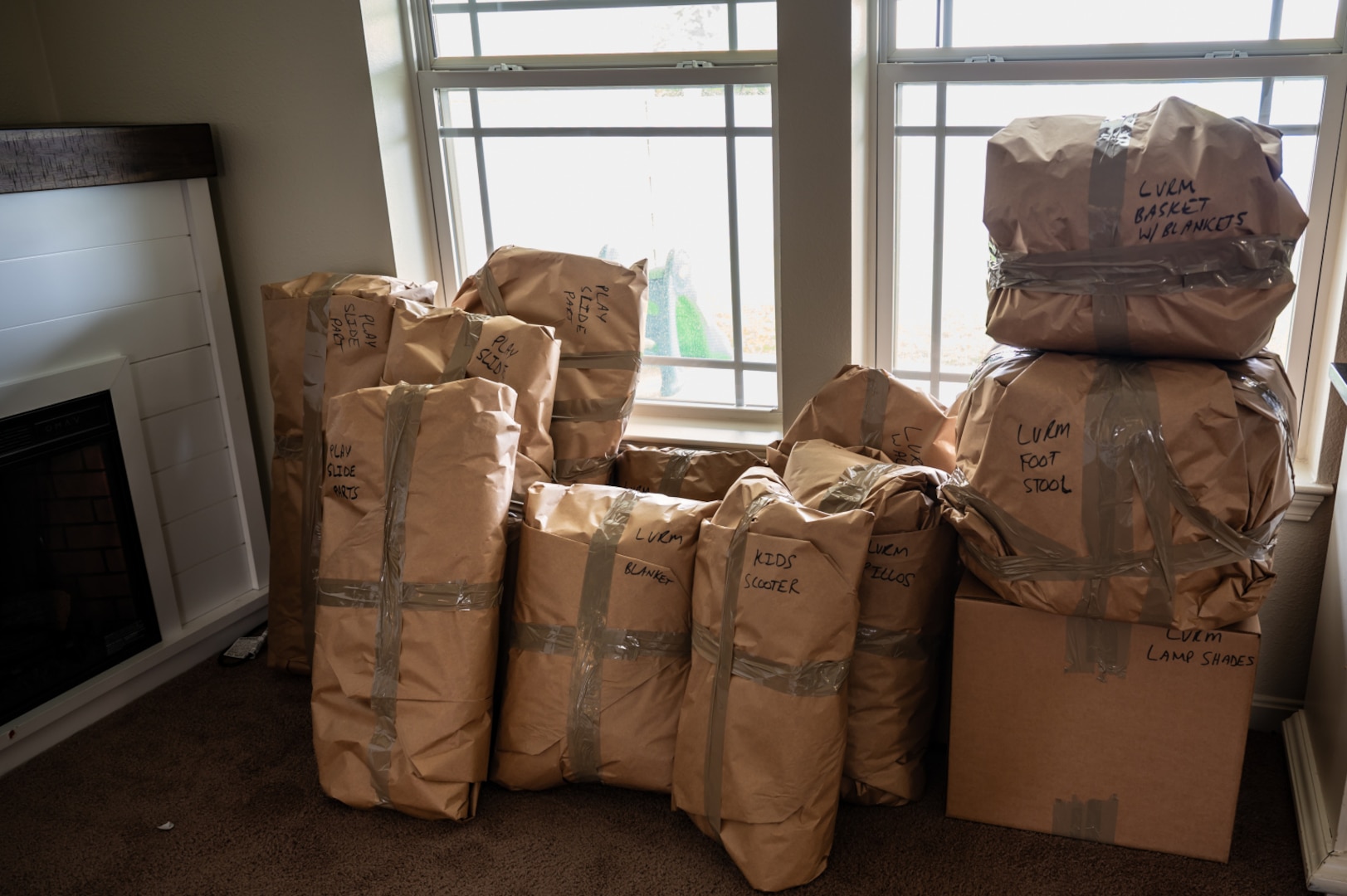 Household items wrapped in brown paper and sealed with packing tape sit near a window inside a house.
