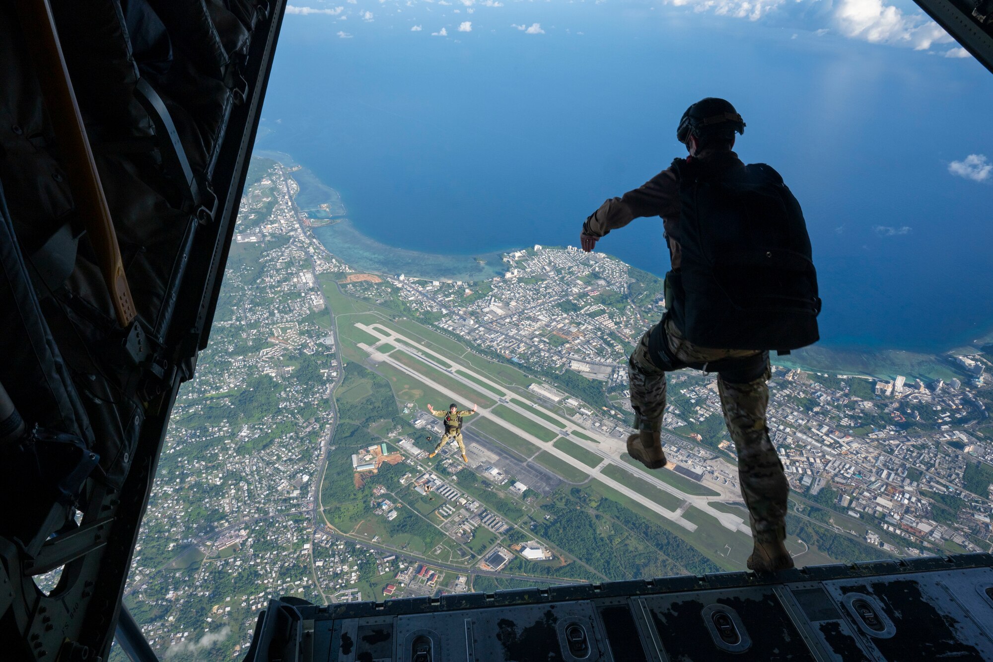 Navy and Marine Corps members jump off the ramp of an aircraft.