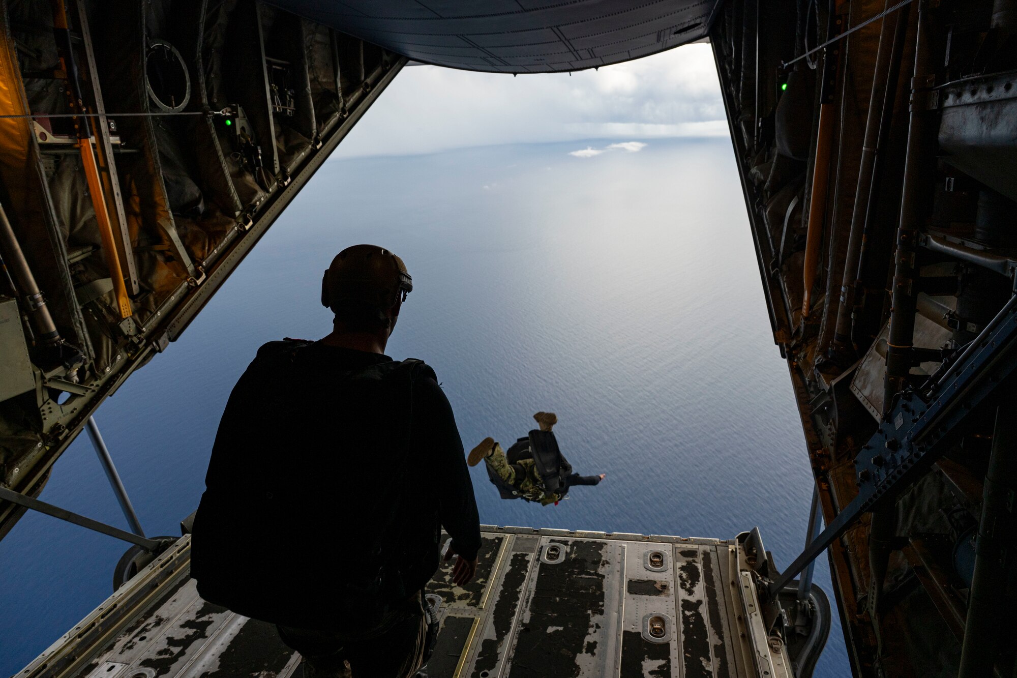 Navy and Marine Corps members jump off the ramp of an aircraft.