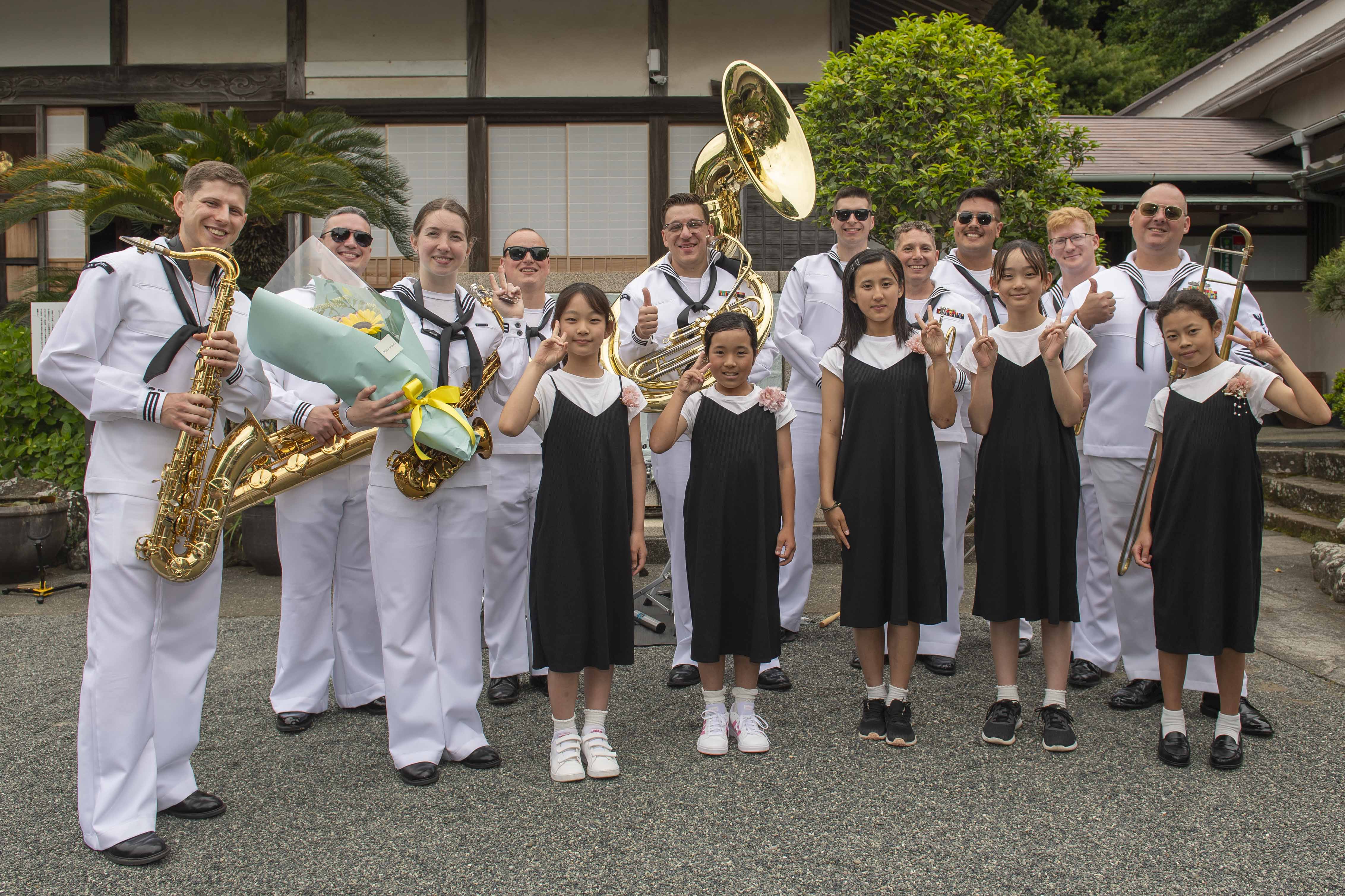 U.S. Navy Sailors assigned to 7th Fleet Band pose for a group photo with 5 girls after receiving a gift of flowers during the 86th Annual Shimoda Black Ship Festival’s Gyokusenji Temple Memorial ceremony.