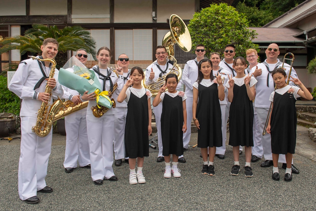 U.S. Navy Sailors assigned to 7th Fleet Band pose for a group photo with 5 girls after receiving a gift of flowers during the 86th Annual Shimoda Black Ship Festival’s Gyokusenji Temple Memorial ceremony.
