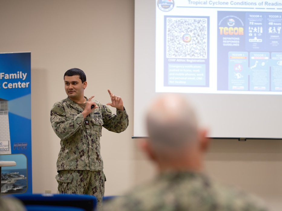 Damage Controlman 2nd Class Joshua Roman assigned to the Commander, Fleet Activities Yokosuka (CFAY) Emergency Operations Center, pauses to allow members of the audience to scan a QR code to register for the installation's emergency notification system while discussing the Tropical Cyclone Conditions of Readiness, or TCCOR.