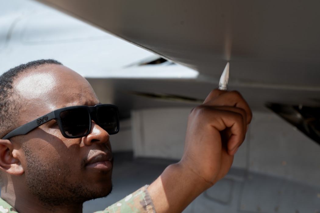 Airman uses a tap hammer on a wing of an F-16