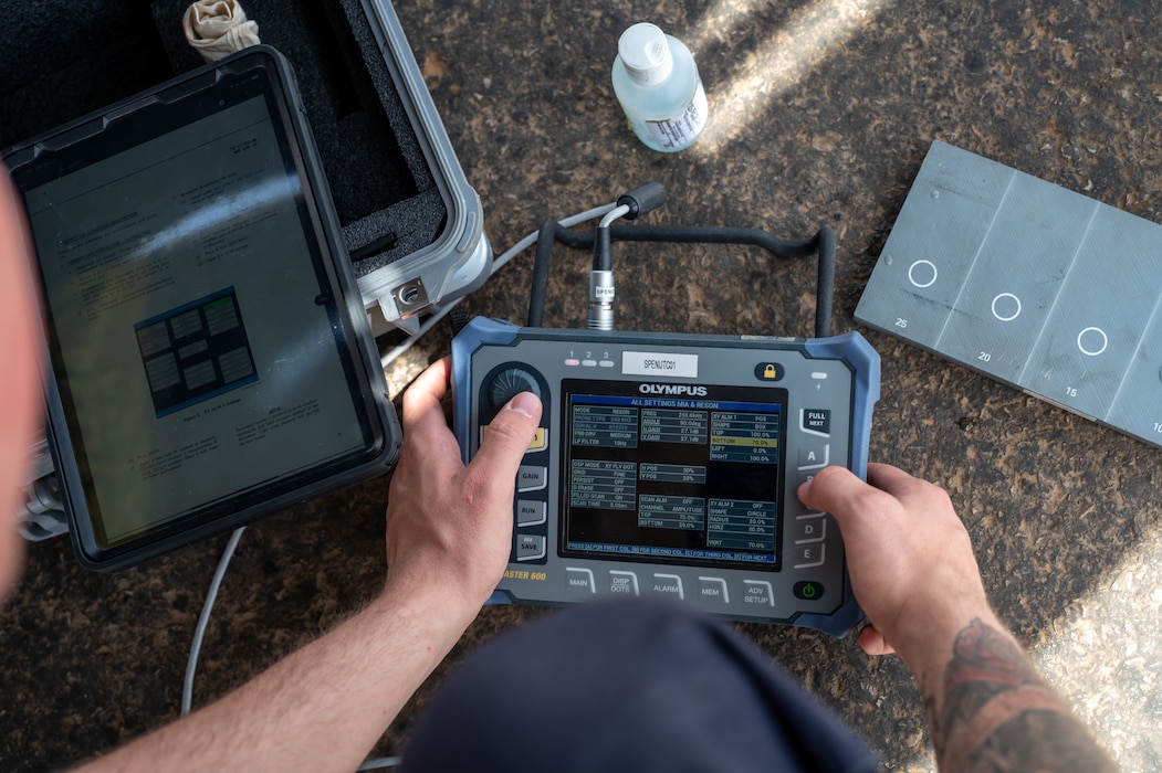 Airman powers on an ultrasonic unit while looking at a technical order on an iPad