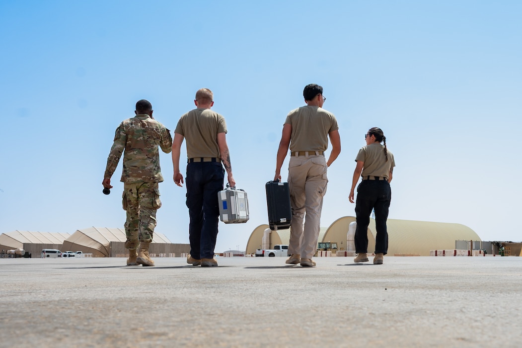 Four Airmen walk across a flightline