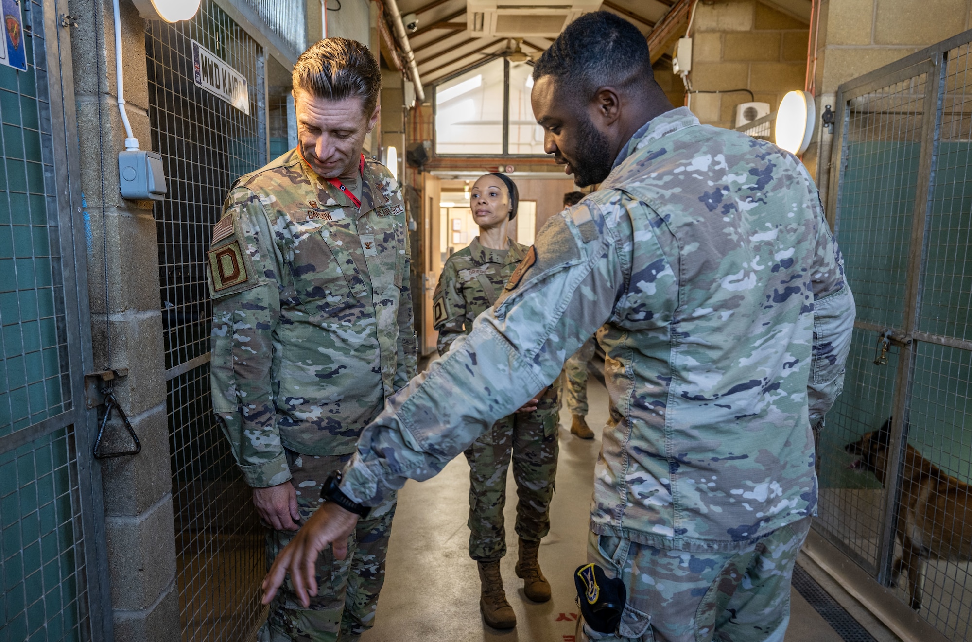 U.S. Air Force Senior Airman Jelani Bell, right, 100th Security Forces Squadron military working dog handler, explains to Col. Ryan Garlow, left, 100th Air Refueling Wing commander, and Chief Master Sgt. Tiffany Griego, 100th ARW command chief, how to properly clean out the military working dog kennels during a Day in the Life integration with the 100th SFS at RAF Mildenhall, England, May 30, 2025.