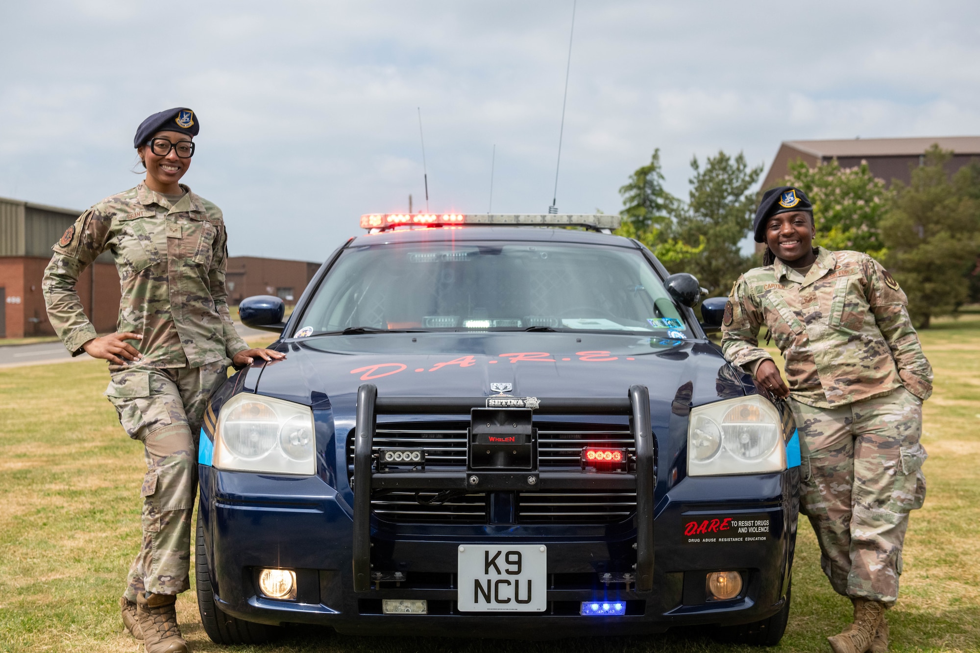 Two defenders pose in front of a police car