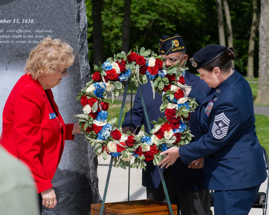 A woman in a red jacket and a woman in uniform in place a wreath on a three-legged easel.