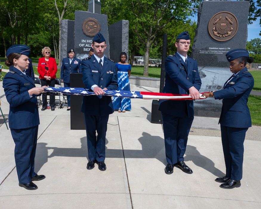Two men and two women in uniform stand at attention as they fold the American Flag.