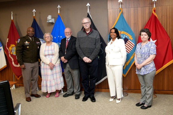 Six people stand in front of flags.