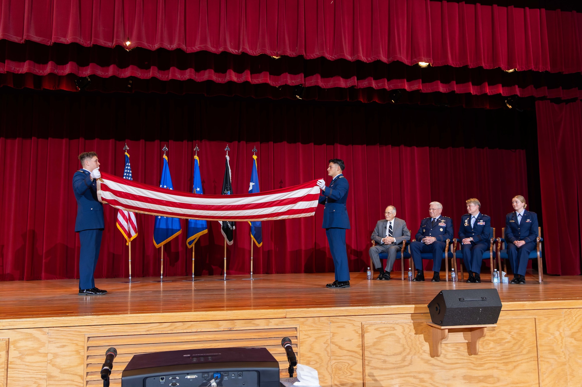 A photo of a flag being folded in half, on stage, while Brig. Gen. Linell Letendre and her official party watch.
