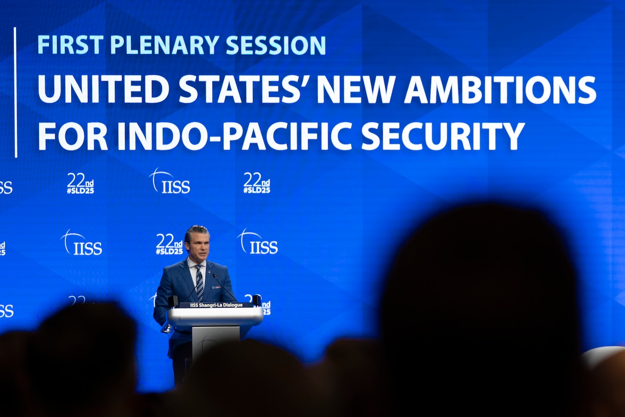 A man in a suit stands in front of a lectern and an audience with a blue background and screen that reads United States' New Ambitions for Indo-Pacific Security.