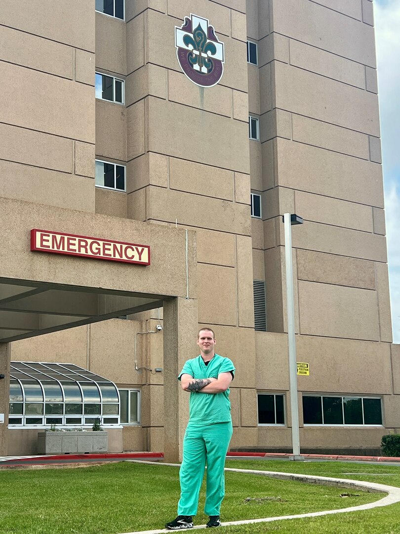 Soldier in scrubs standing in front of hospital entrance.
