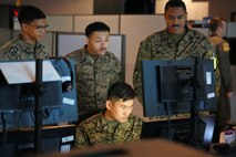 four uniformed U.S. Marines look at a computer screen