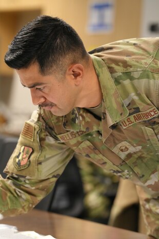 uniformed U.S. Air Force Airman look at maps on table.