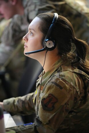 uniformed US Air Force Airman wearing a headset works on a computer