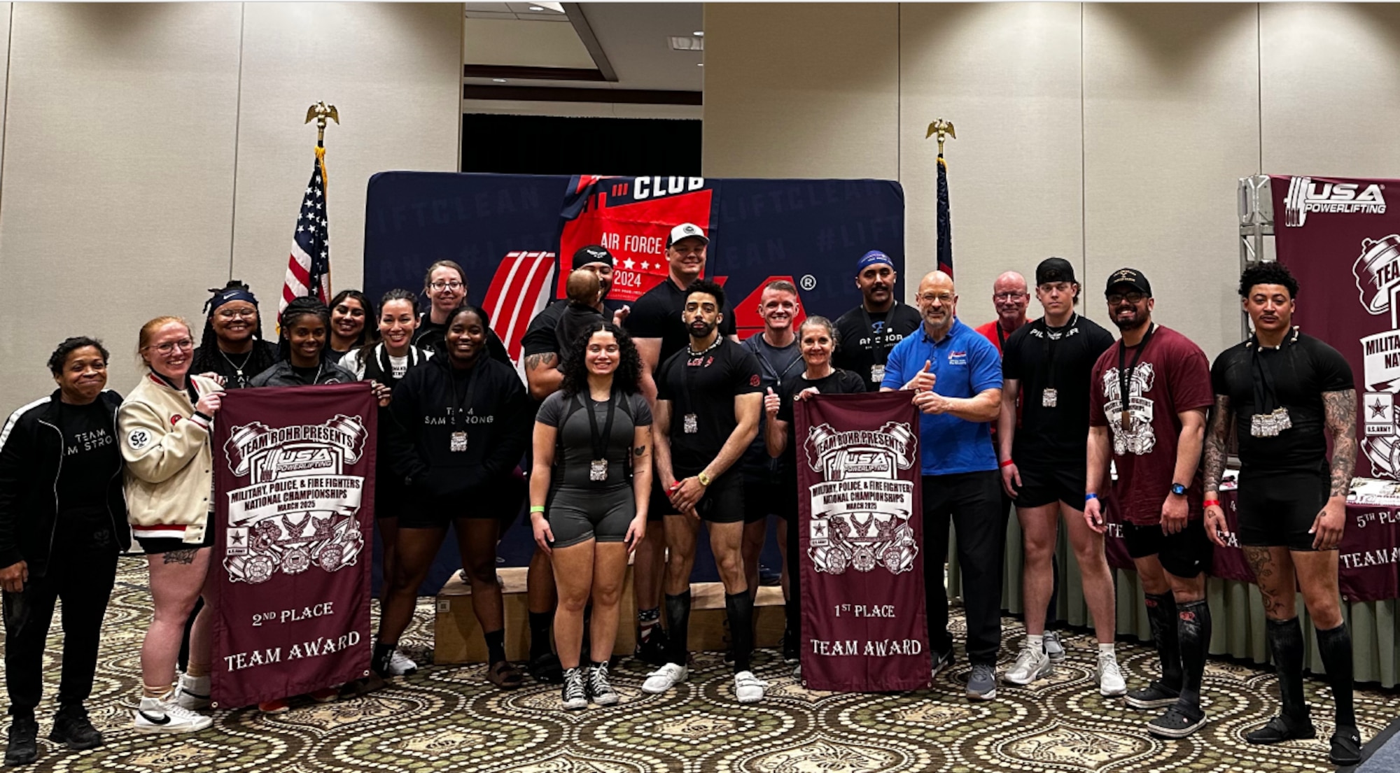 Air Force and Firefighting teams pose together with their championship banners at the USA Powerlifting Military, Police, & Firefighter's Nationals
