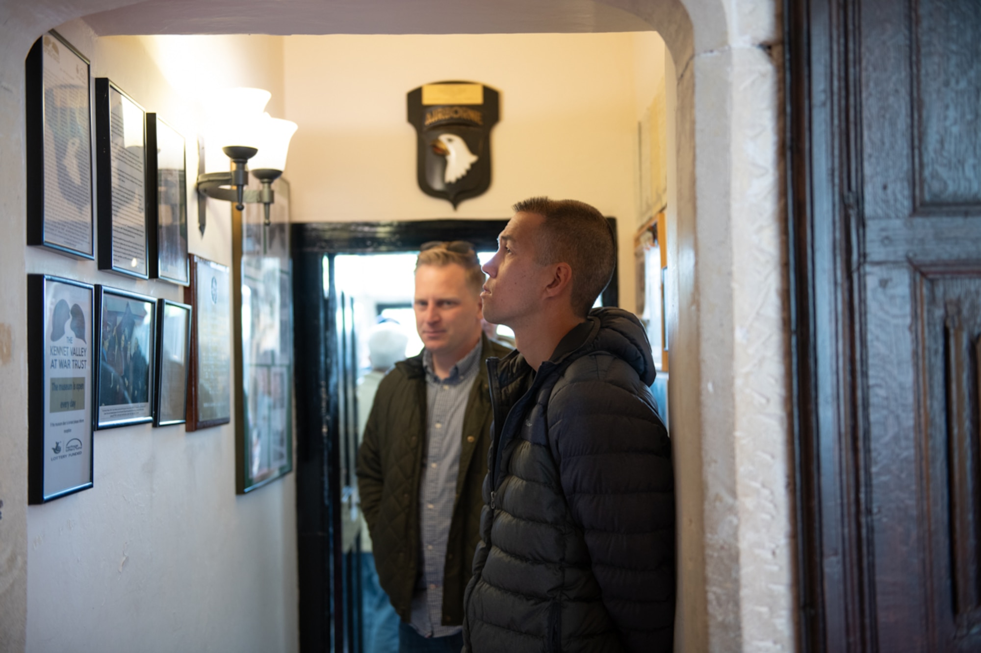 Airmen standing in a museum looking at the wall of historic artifacts of the grounds used during D-Day.