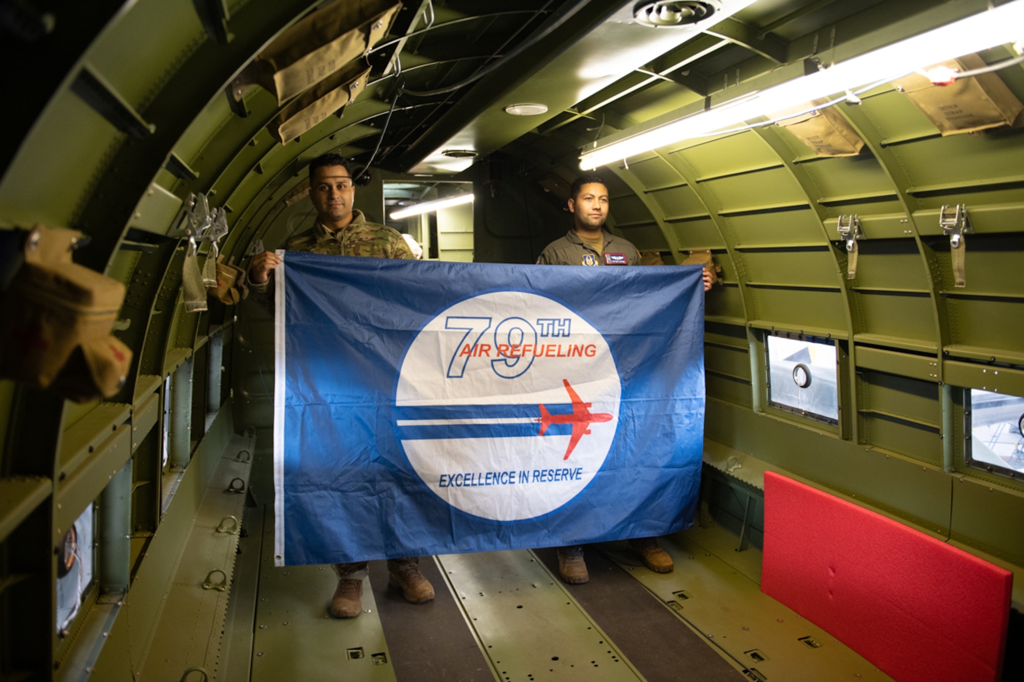 Two Airmen standing side by side inside the C-47 Night Fright holding a 79th squadron flag.