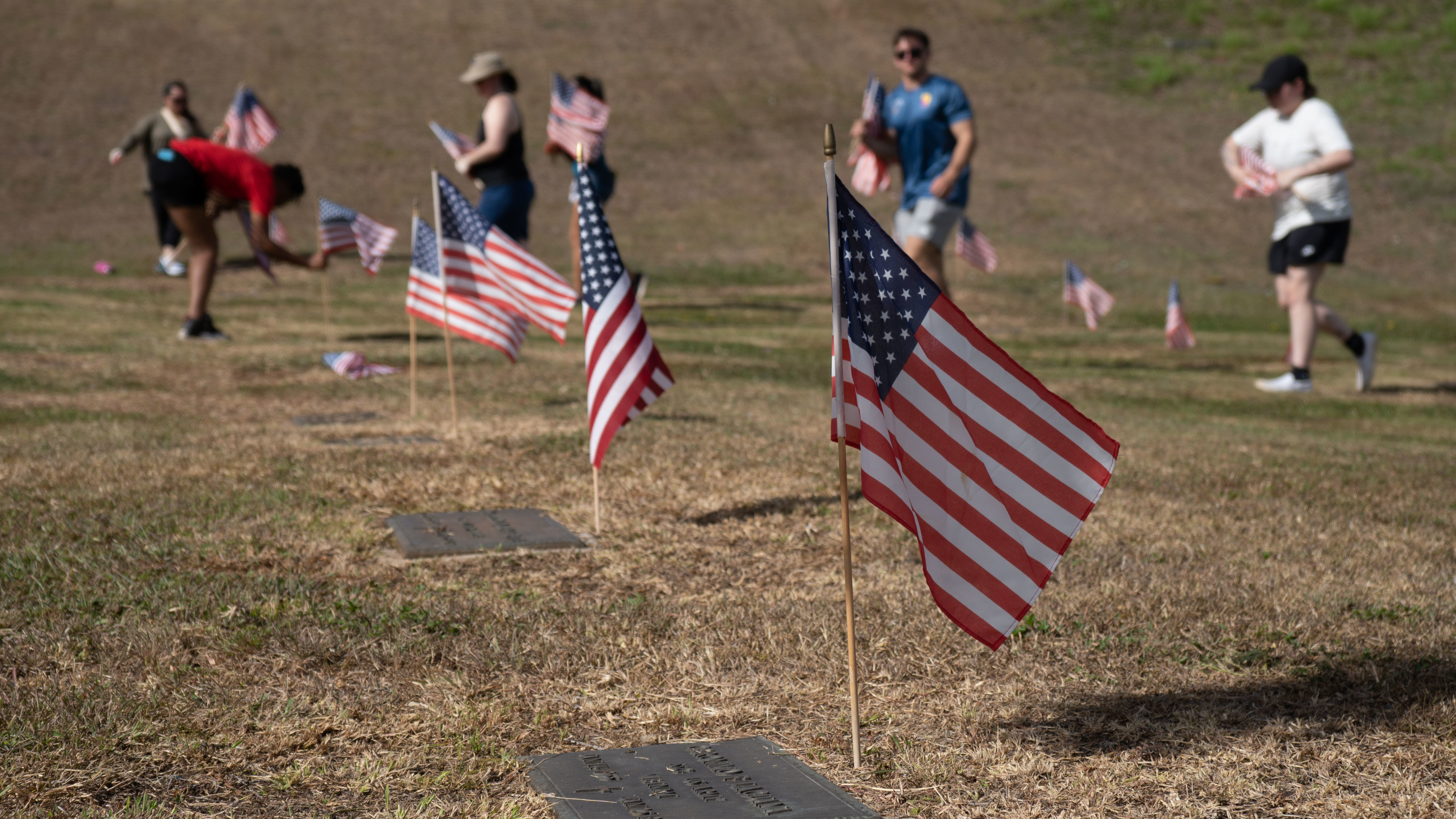 U.S. Marines and volunteers place flags at the top of veterans’ headstones in preparation for Memorial Day at Guam Veterans’ Cemetery, Piti, Guam, May 24, 2025.  During the Saturday before Memorial Day volunteers assisted the cemetery staff with placing American flags for the service members that are laid to rest here. (U.S. Marine Corps photo by Lance Cpl. Afton Smiley)
