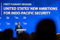 A man in a suit stands in front of a lectern and an audience with a blue background and screen that reads United States' New Ambitions for Indo-Pacific Security.