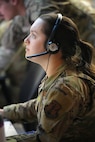 uniformed US Air Force Airman wearing a headset works on a computer