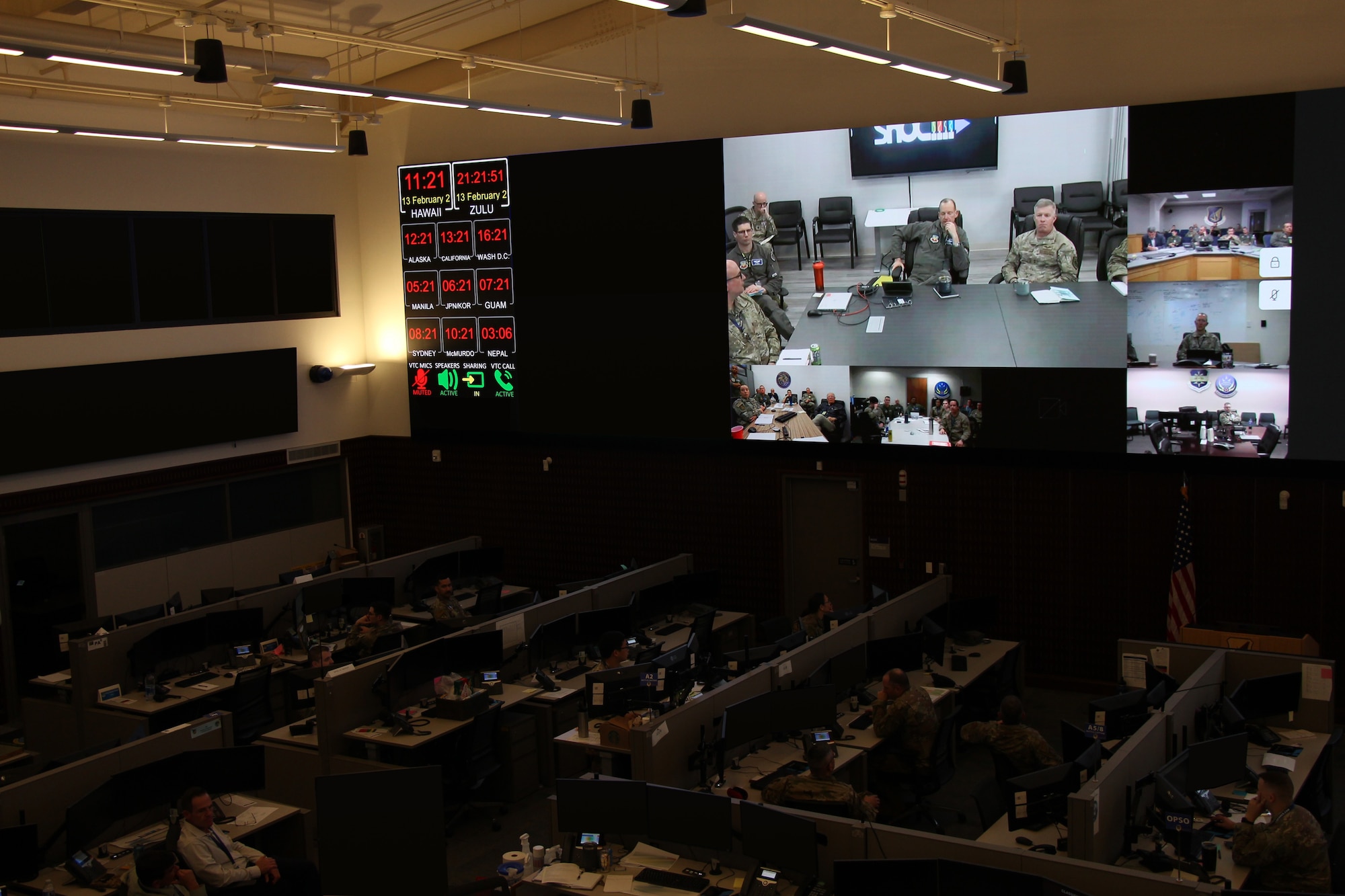 photo of a large room with cubicles and people working and a large projector with multiple screens.