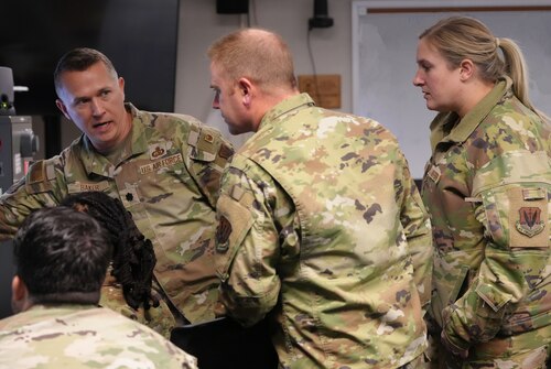 uniformed U.S. Air Force Airmen discuss what they are seeing on the computer screen