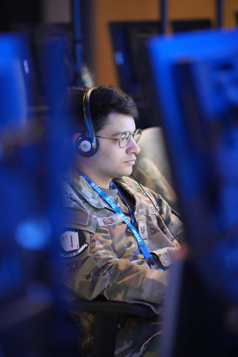 uniformed U.S. Air Force Airman wearing a headset and glasses looks at a computer screen