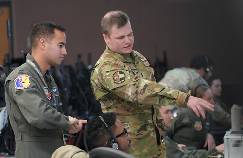uniformed US Air Force military members stand discussing what they are looking at on a computer screen
