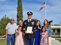 A male Soldier in dress uniform poses for a picture with his family after his promotion ceremony. Ceremony was outside on a sunny day.