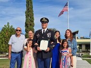 A male Soldier in dress uniform poses for a picture with his family after his promotion ceremony. Ceremony was outside on a sunny day.