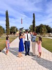 Wife and daughters of male Soldier pin his rank during his promotion ceremony. Ceremony is outside on a sunny day.