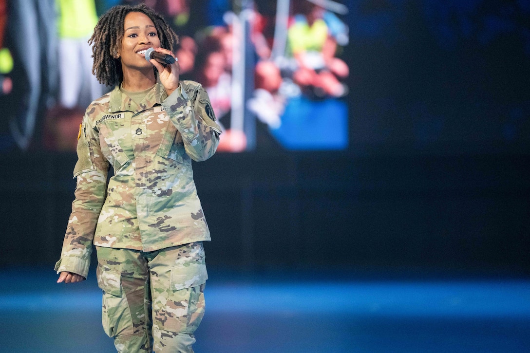 A soldier standing in uniform and holding up a microphone sings.