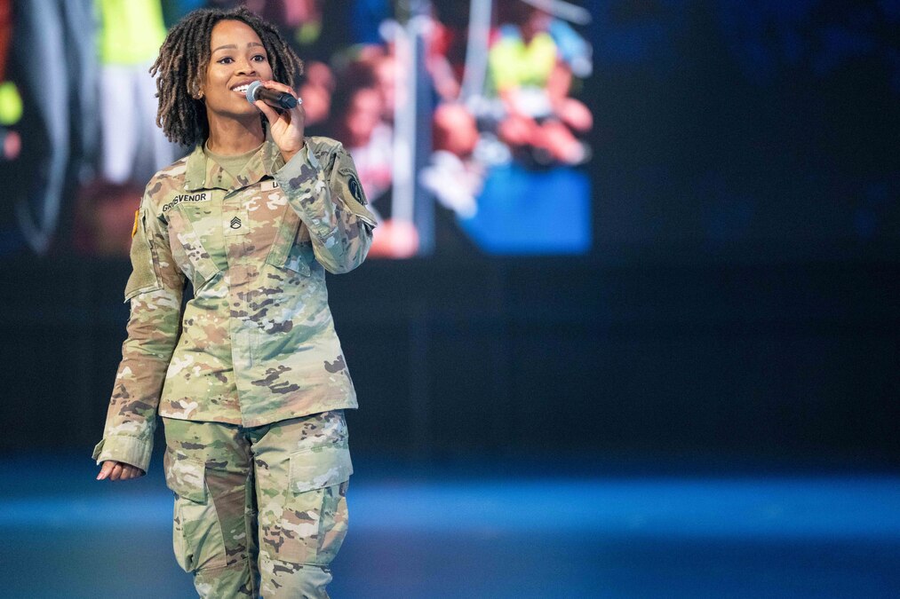 A soldier standing in uniform and holding up a microphone sings.