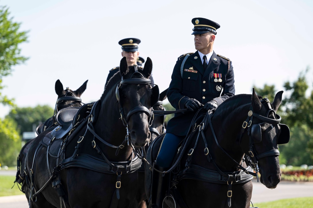 Two soldiers in ceremonial dress ride horses while holding the reins of a neighboring horse against a blue sky.
