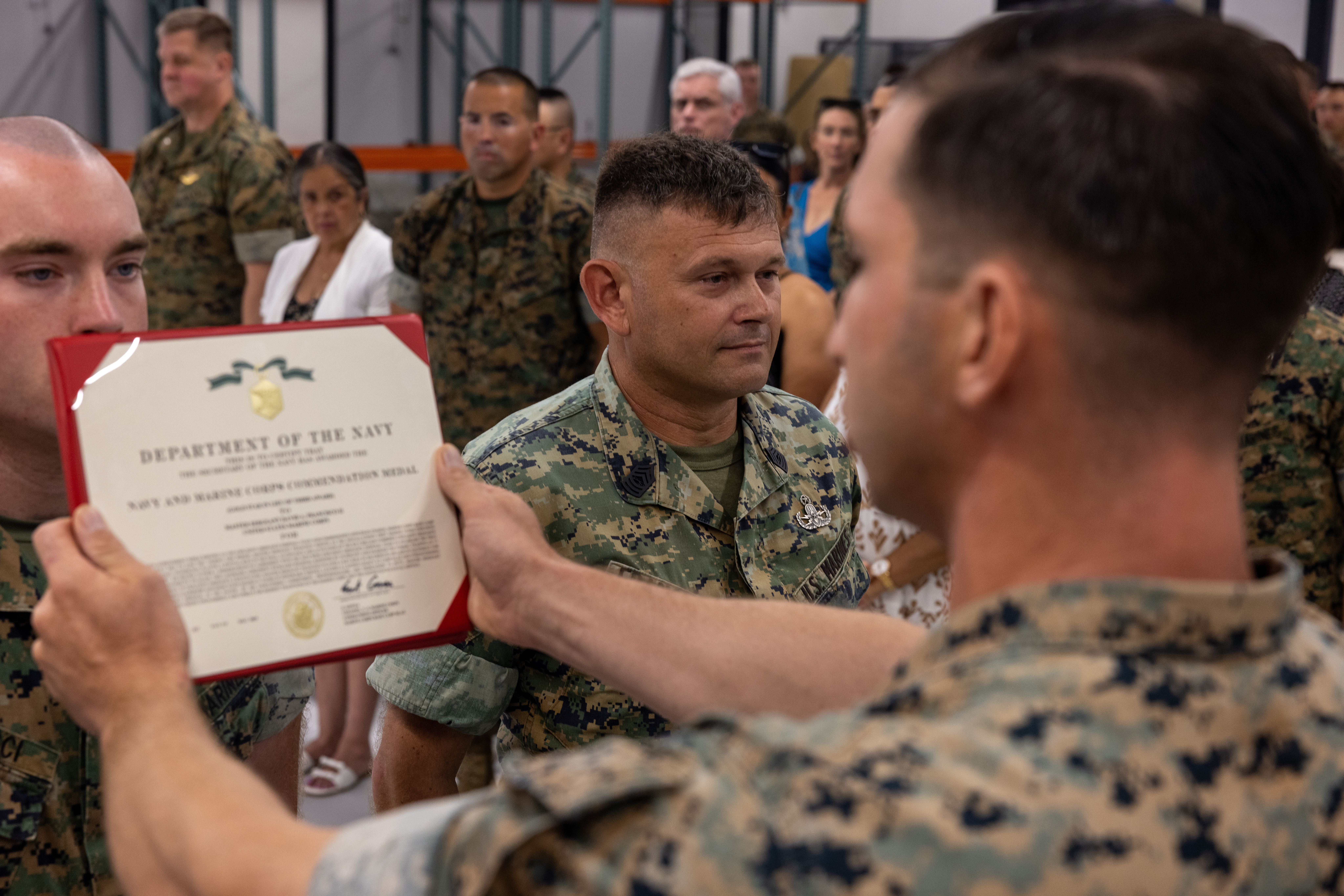 U.S. Marine Corps Gunnery Sgt. Nicholas Raetz, explosive ordnance disposal technician, Headquarters Company, Marine Corps Base Camp Blaz, reads an award presented to Master Sgt. David Francisco, explosive ordnance disposal technician, HQ Co, MCB Camp Blaz, during his retirement ceremony on MCB Camp Blaz, Guam, May 30, 2025. Master Sgt. Francisco retired after 21 years of faithful service to the Marine Corps. (Marine Corps photo by Cpl. Ryan Little)