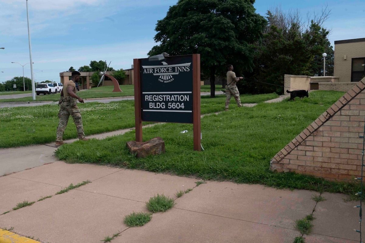 Two military working dog teams pass behind a sign that says "Air Force Inns, registration, Building 5604
