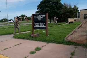 Two military working dog teams pass behind a sign that says "Air Force Inns, registration, Building 5604
